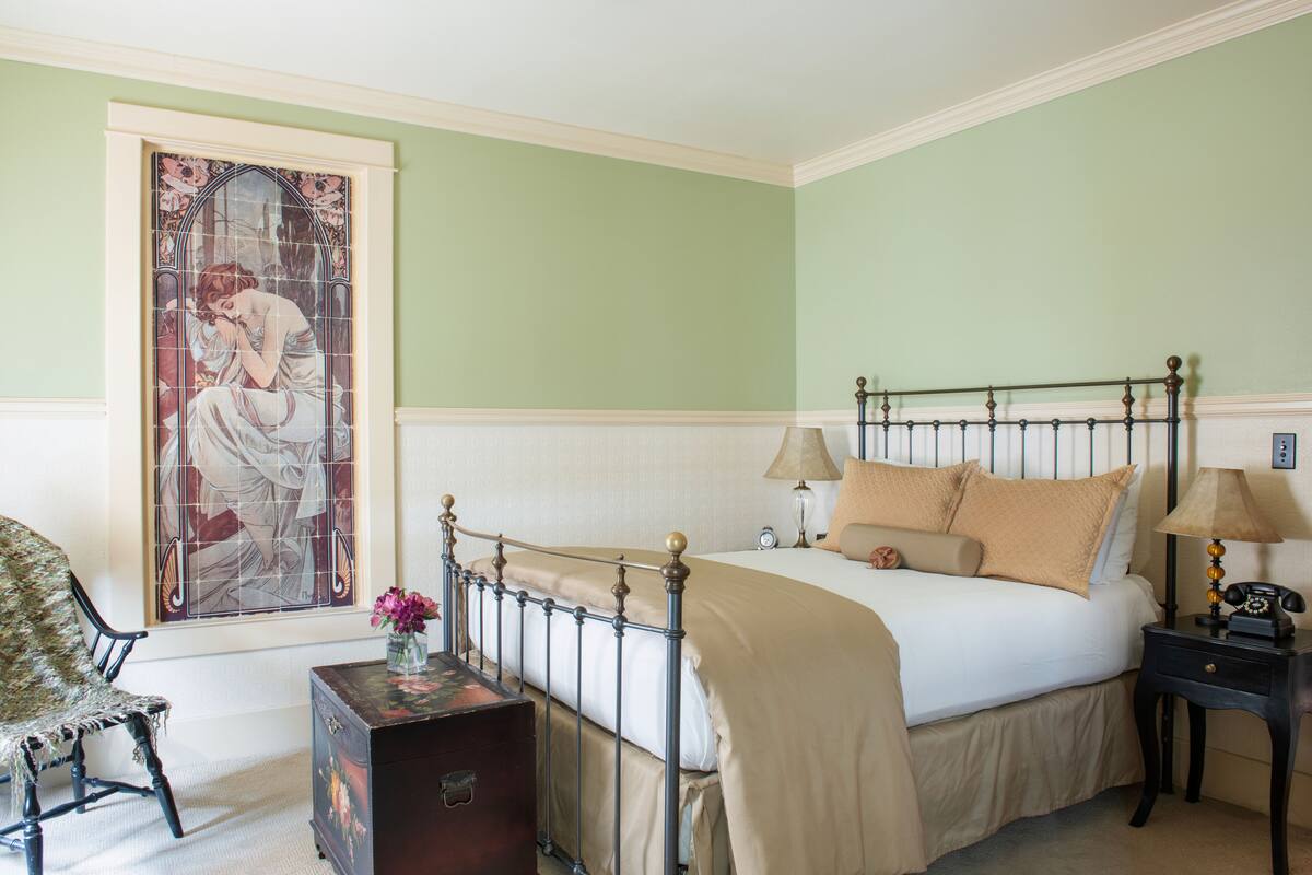 A bedroom with a bed, bedside tables, a chair, and a large stained glass window.