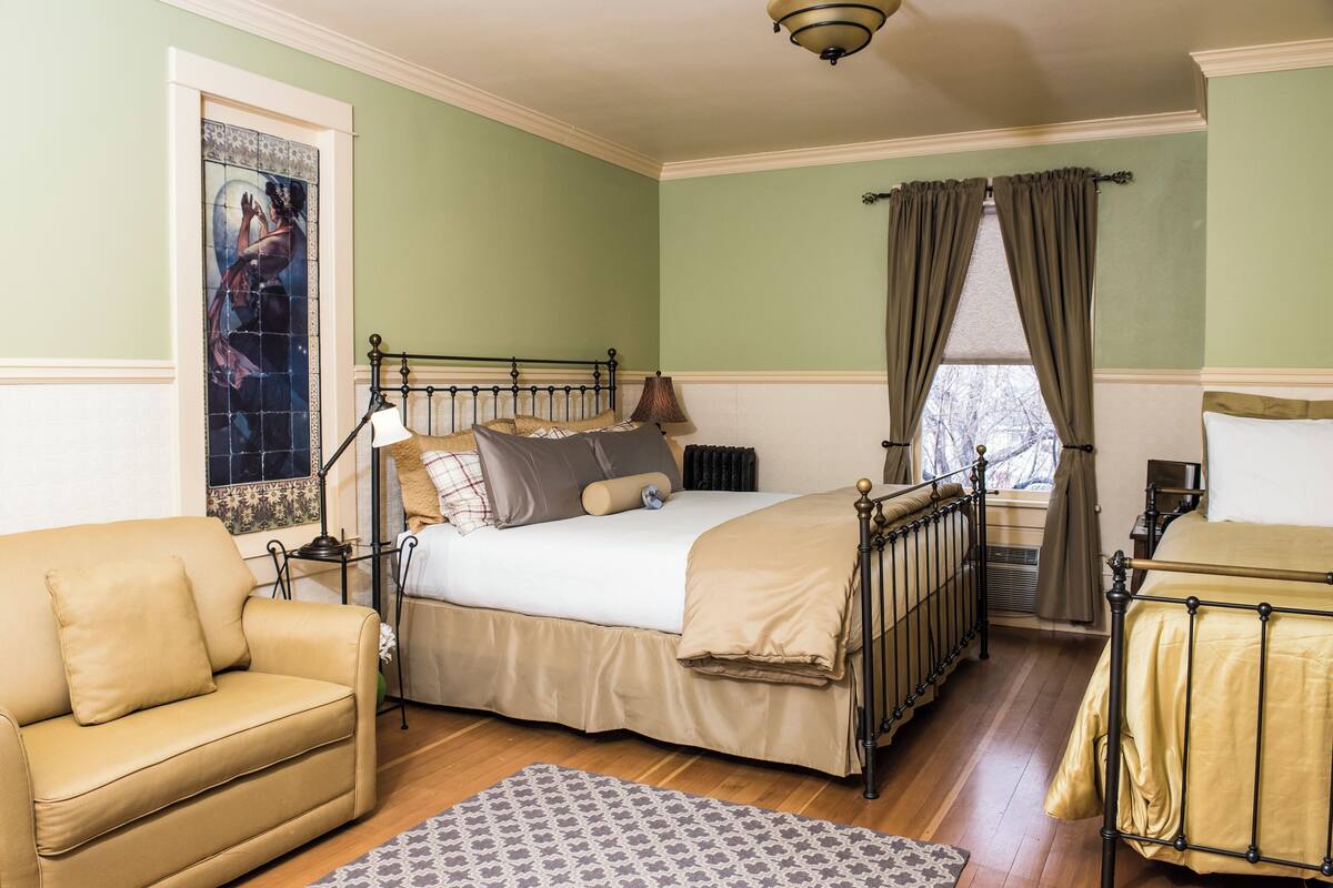 A bedroom with a bed, a chair, a window with curtains, and a radiator.