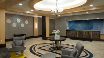 A lobby with a reception desk, two armchairs, a coffee table, and a chandelier.