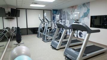 Een sportschool met loopbanden, fitnessballen en een spiegelwand.