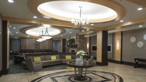 A modern lobby with a central round table, a sectional sofa, and a chandelier.