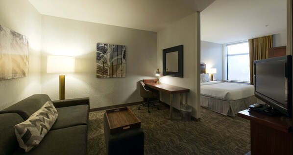 A hotel room with a sofa, a desk, a bed, a television, and artwork on the walls.