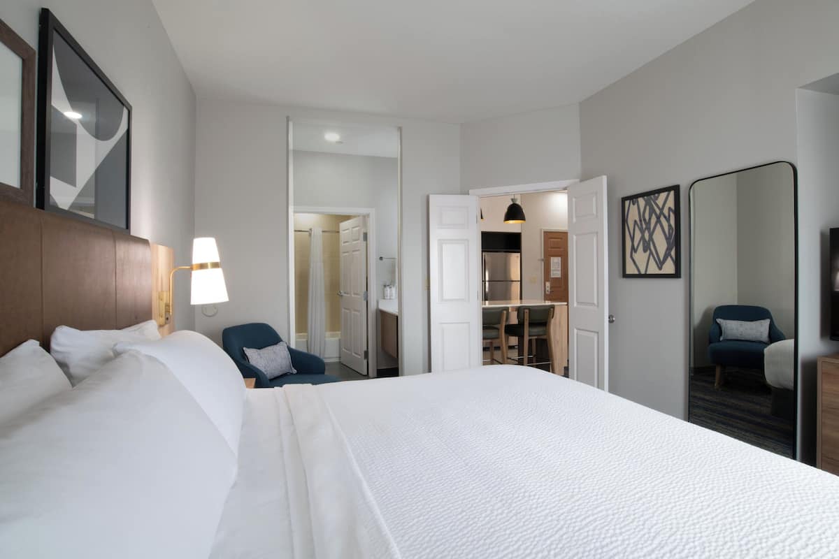 A hotel room with a large bed, a desk, a chair, and a wardrobe.