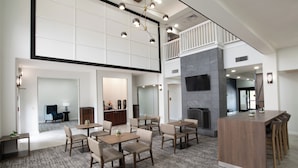 Un grand espace à manger avec plusieurs tables et chaises, un îlot central doté de tabourets de bar et un plafond haut orné d’un motif en forme de grille.