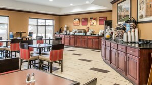 Un comedor de hotel con mesas y sillas, una estación de café y un amplio ventanal que proporciona luz natural.