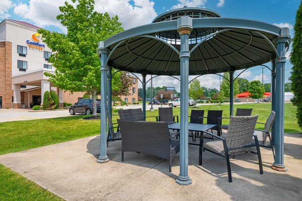 Um gazebo com área de estar externa, um hotel Comfort Suites ao fundo e um gramado bem cuidado.