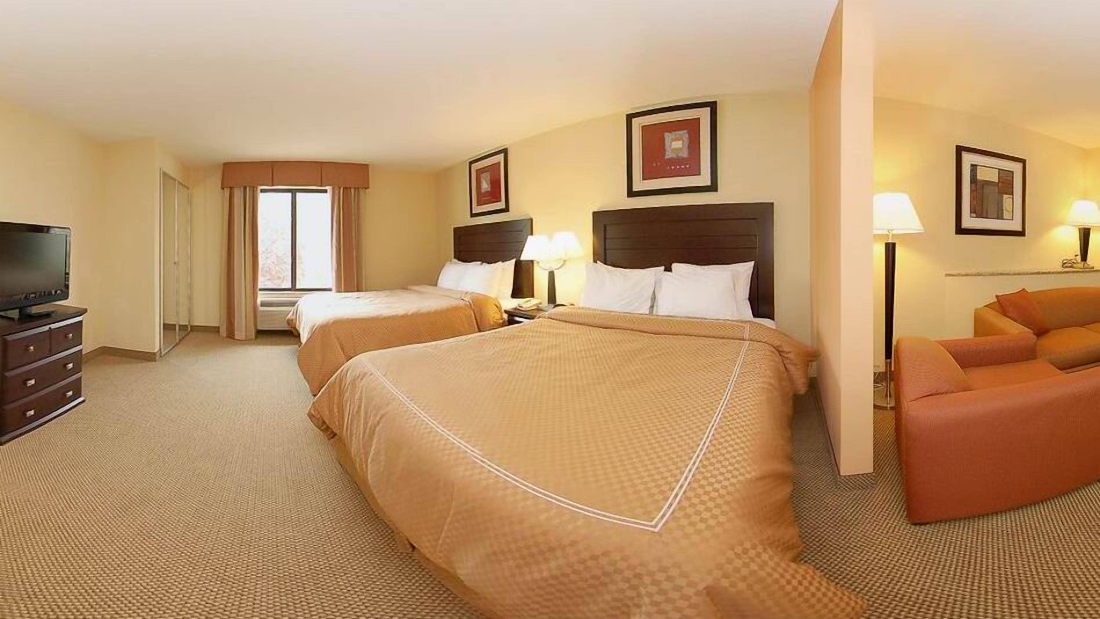 Una habitación de hotel con dos camas, televisión, escritorio y sofá.