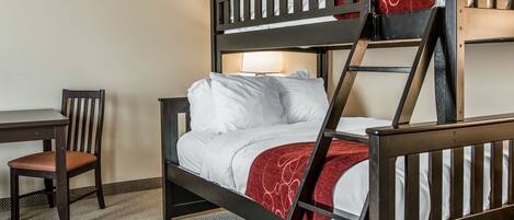 A bunk bed with a desk and chair, a lamp, and a patterned rug.