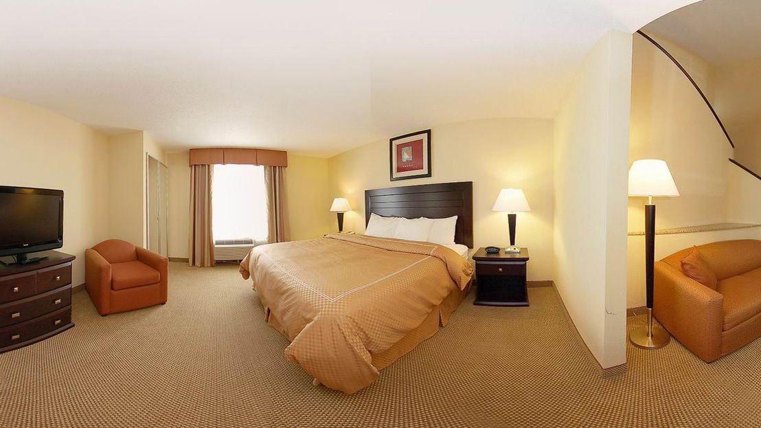 A hotel room with a large bed, two bedside tables with lamps, a television, a sofa, and a desk.