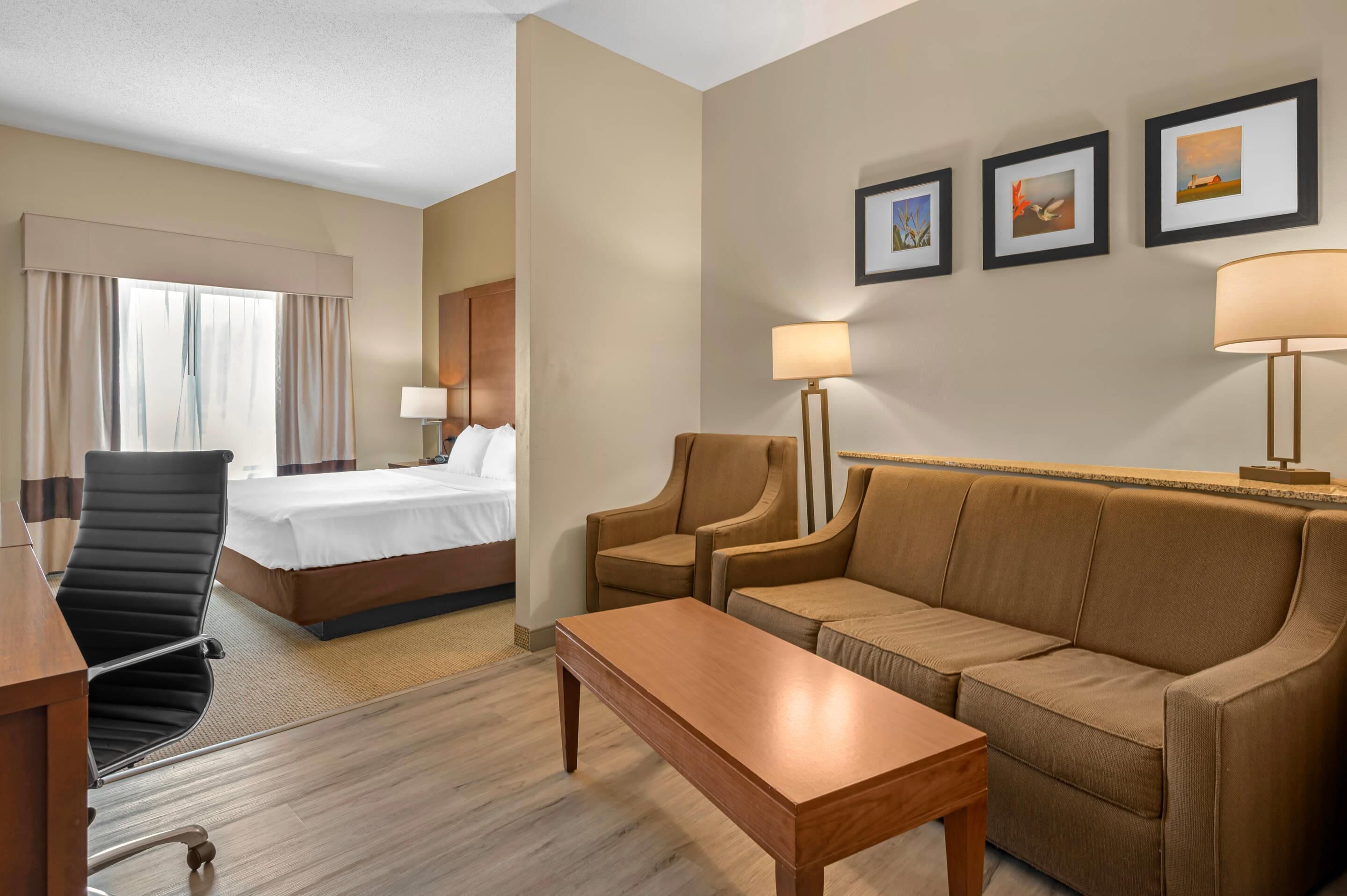 A hotel room with a bed, a desk, a sofa, a coffee table, and a lamp. There are three framed pictures on the wall.