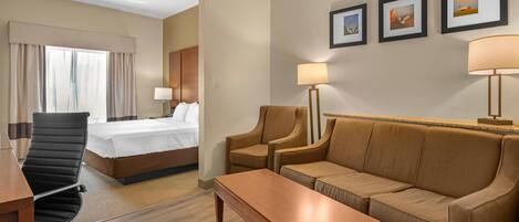 A hotel room with a bed, a desk, a sofa, a coffee table, and a lamp. There are three framed pictures on the wall.