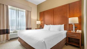 A hotel room with a large bed, two bedside tables with lamps, a window with curtains, and a wooden headboard.