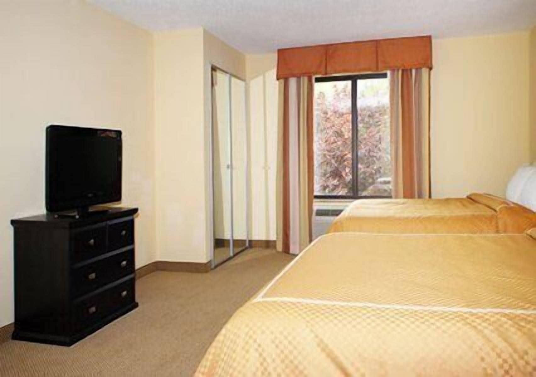 Una habitación de hotel con una cama, un televisor sobre una cómoda y una ventana con cortinas.