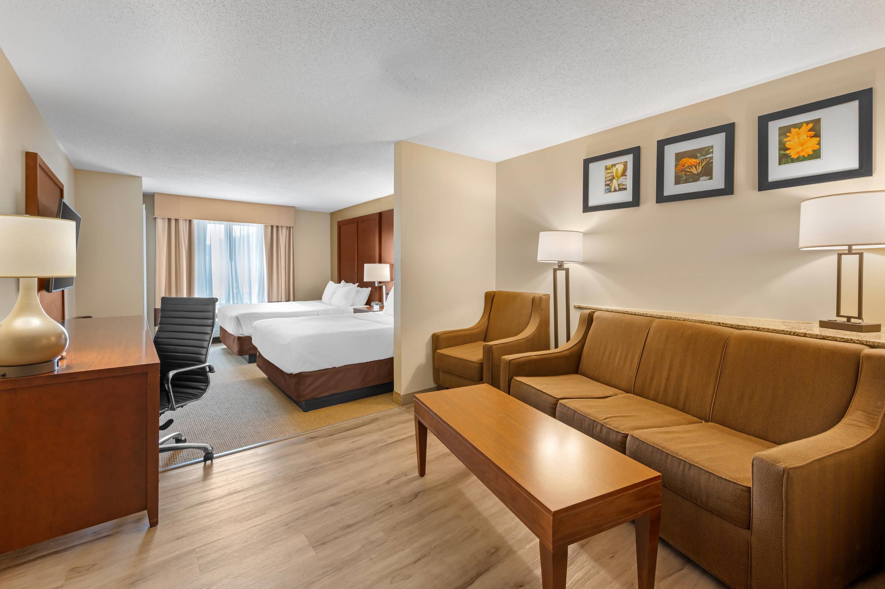 A hotel room with a bed, two bedside tables, a sofa, a desk, and a chair. There are three framed pictures on the wall.
