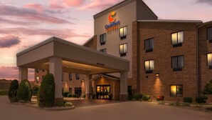 Un hotel Comfort Suites con fachada de ladrillo, un acceso cubierto y un camino de entrada arbolado.