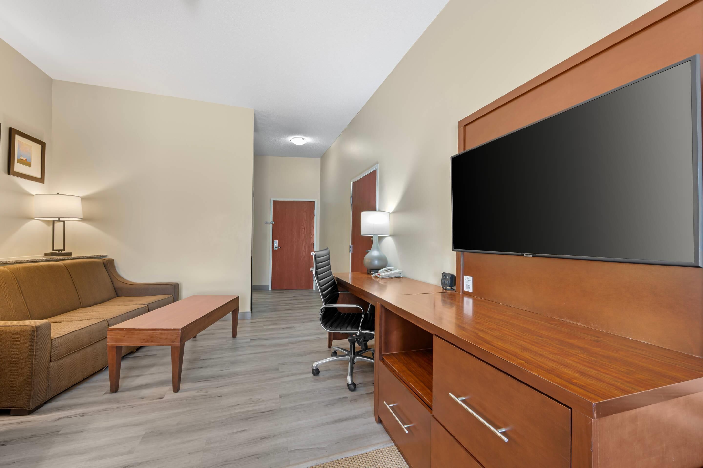 A hotel room with a sofa, a wooden desk, a chair, a television, and a lamp.
