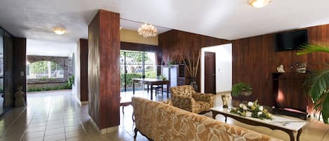 A spacious living area with a sofa set, a dining table, and a TV mounted on the wall.