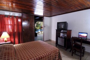 Habitación de hotel con una cama, un escritorio con computadora, televisión y puerta que da a un espacio exterior.