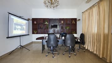 Un salón de conferencias con una pantalla de proyector, un televisor, una araña y un muro decorativo.