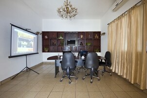 Un salón de conferencias con una pantalla de proyector, un televisor, una araña y un muro decorativo.