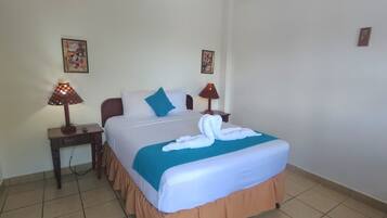 A hotel room with a bed, two nightstands, two lamps, an air conditioner, and two framed pictures on the wall.