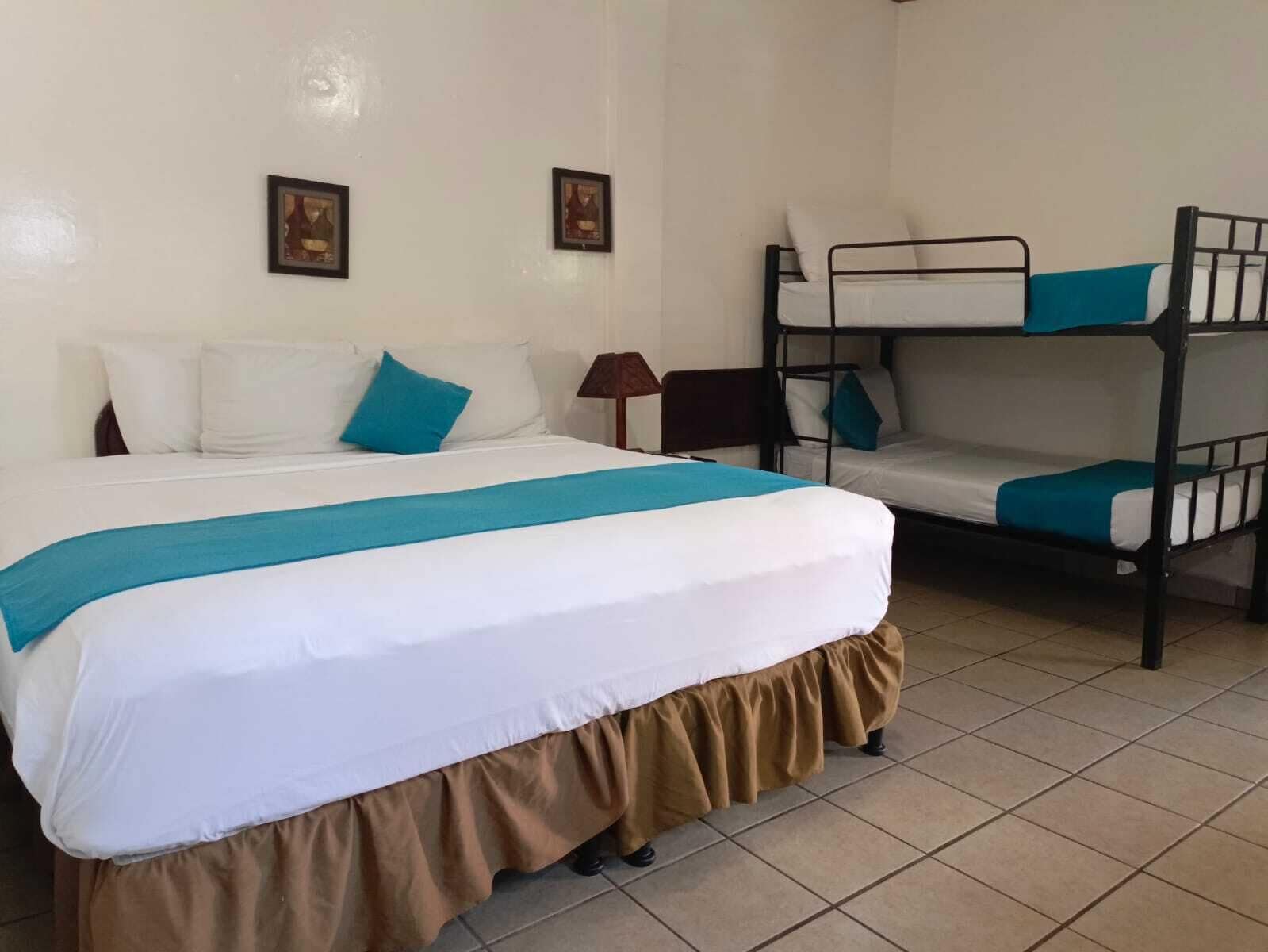 A hotel room with a single bed, a bunk bed, a nightstand, and two wall-mounted pictures.