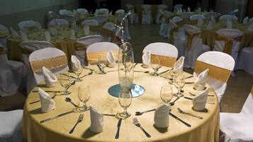 A banquet hall with round tables set for a formal event, each with white tablecloths, gold sashes, and clear glassware.