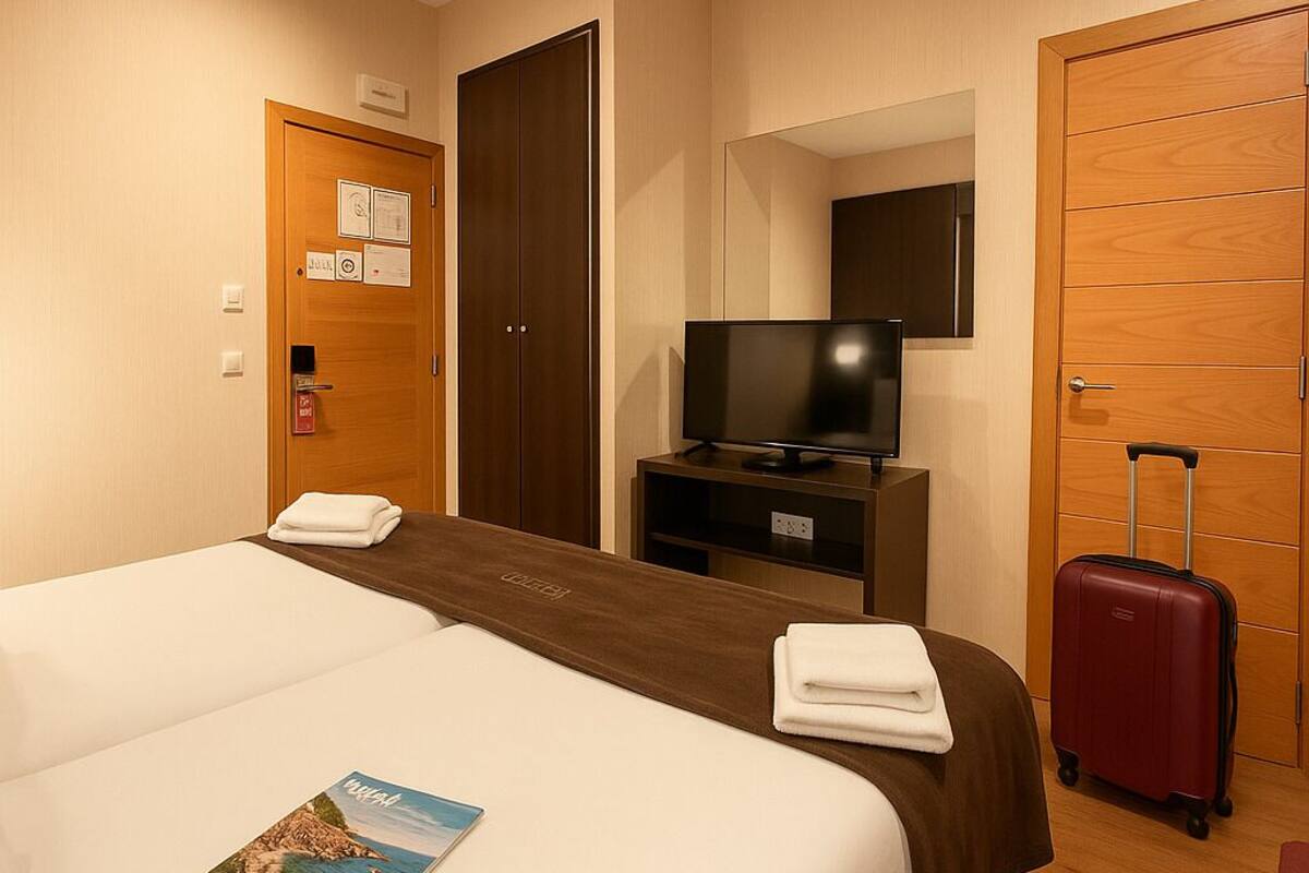 A hotel room with a large bed, a television, a suitcase, and a door with a sign.