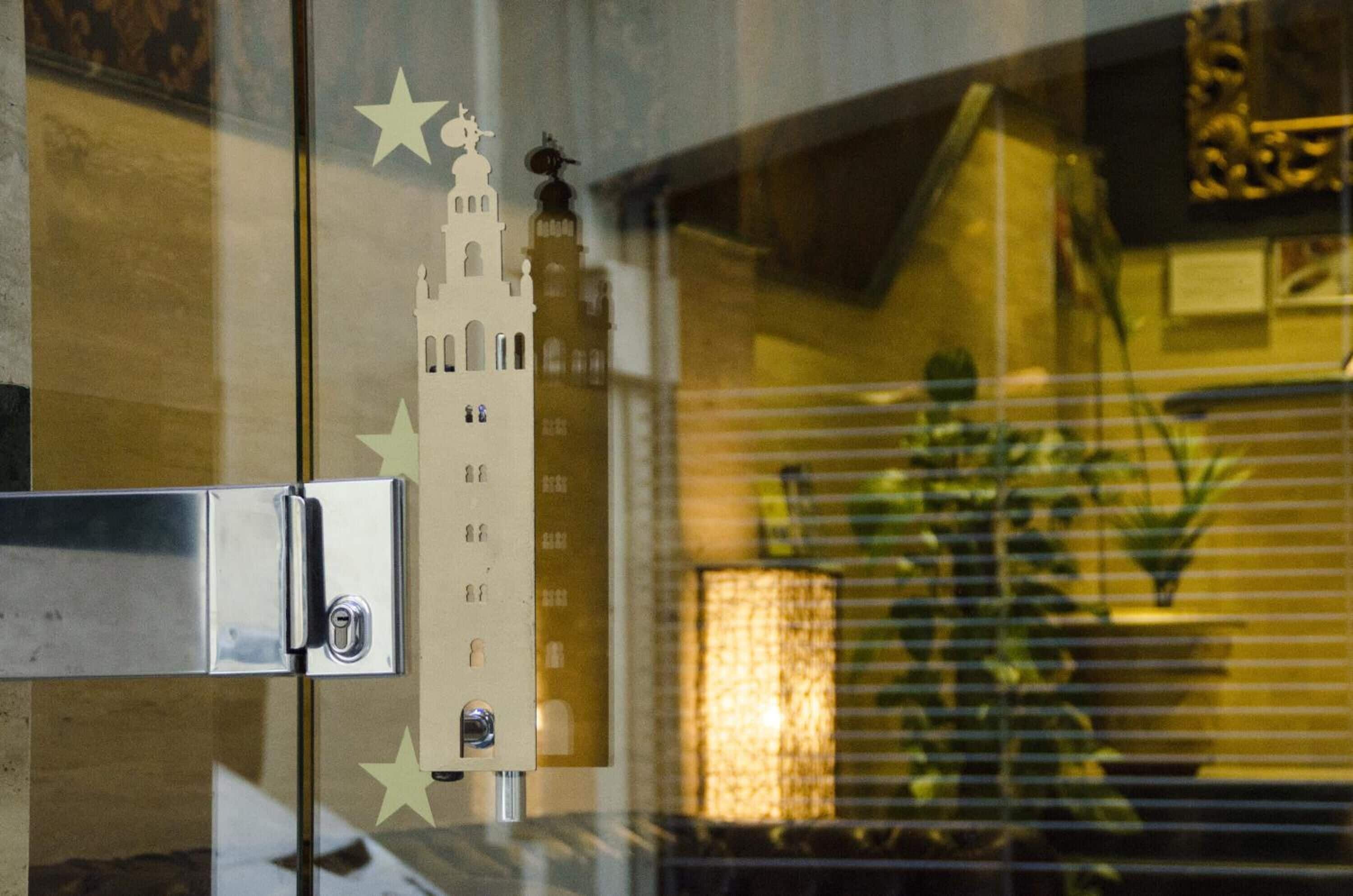 Camera d'hotel con una porta in vetro, serratura a chiave elettronica, una decorazione a forma di stella e il riflesso di un edificio e una lampada.