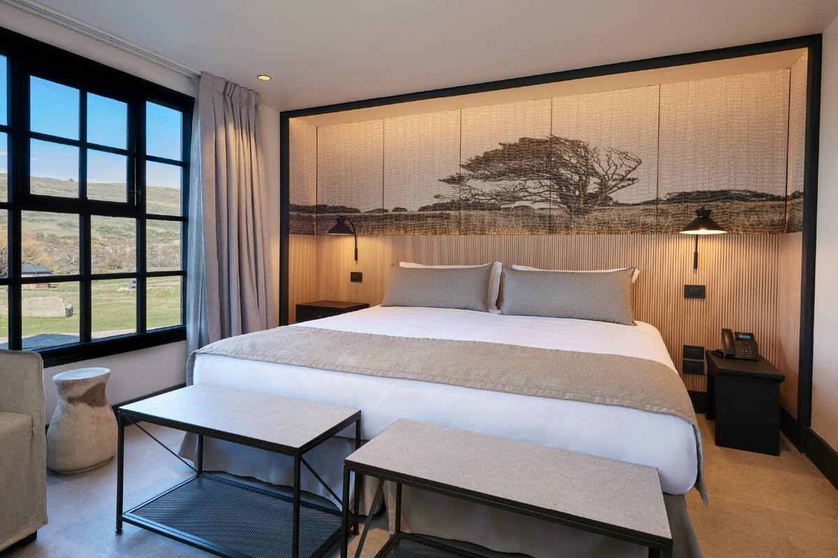 Ein Schlafzimmer mit einem großen Bett, Nachttischen, einem Schreibtisch, einem Stuhl und einem Fenster mit Landschaftsblick.