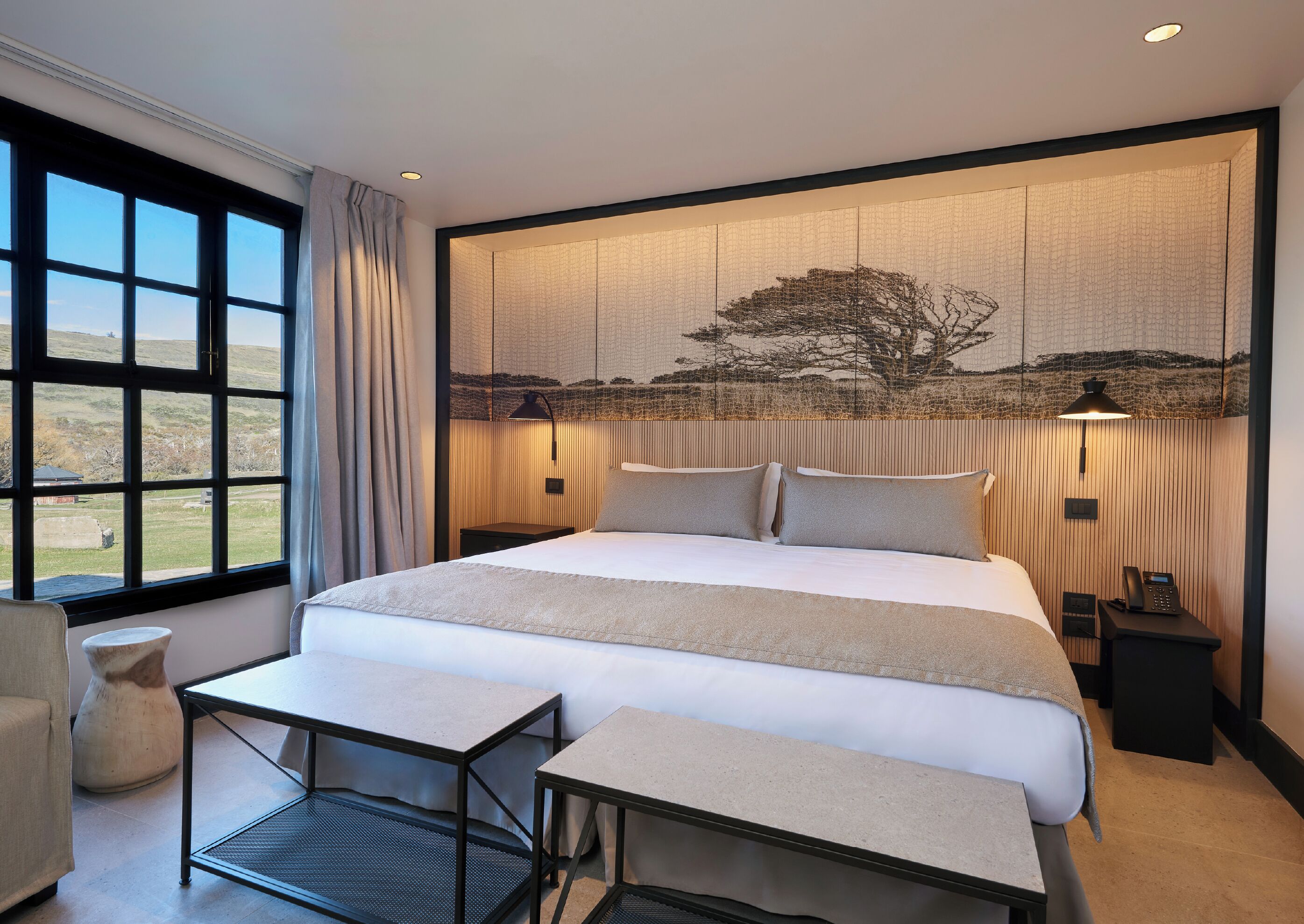 Een slaapkamer met een groot bed, nachtkastjes, een bureau, een stoel en een raam met uitzicht op de omgeving.
