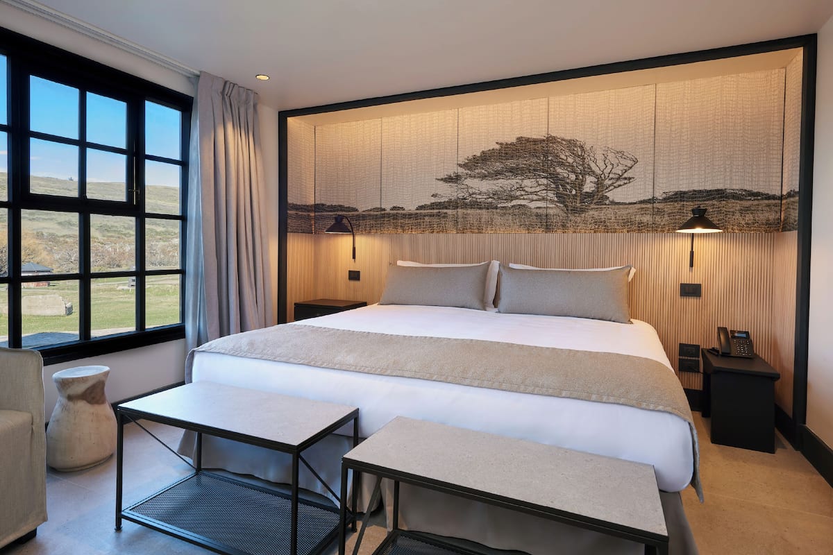 Ein Schlafzimmer mit einem großen Bett, Nachttischen, einem Schreibtisch, einem Stuhl und einem Fenster mit Blick ins Freie.