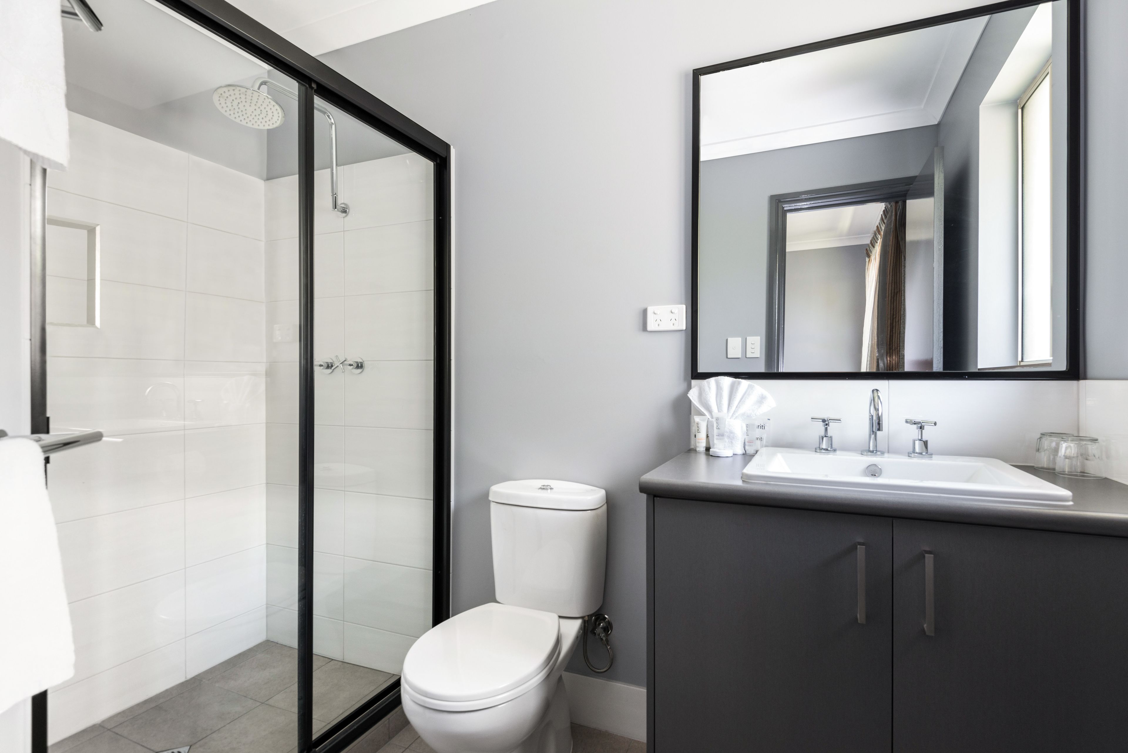 Een moderne badkamer met een douchecabine van glas, een wit toilet en een donkere wastafel met spiegel.