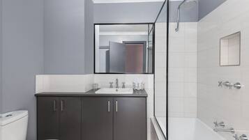 Un baño moderno con un mueble de tocador oscuro, un lavabo blanco y una cabina de ducha de vidrio.