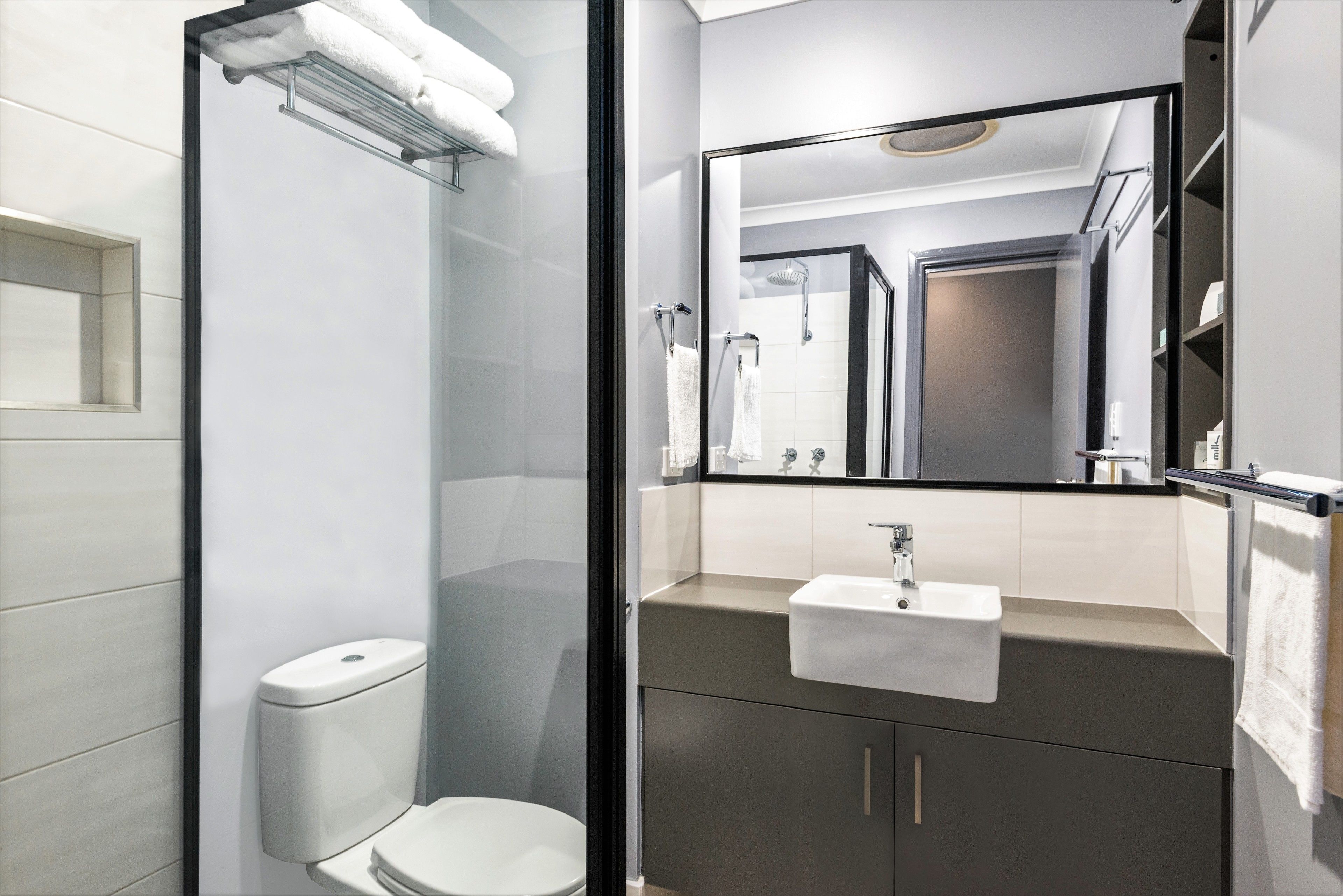 A modern bathroom with a glass-enclosed shower, a white toilet, and a sink with a mirror above it.