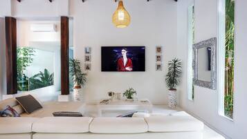 A modern living room with a white sofa, a coffee table, and a TV mounted on the wall. There are two potted plants and a mirror on the wall.