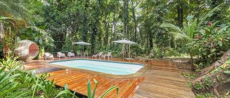 A wooden deck with a pool, surrounded by lush greenery and trees.