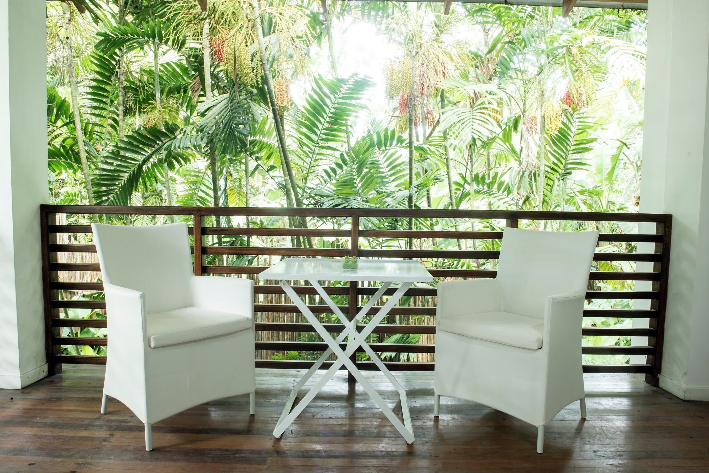 A room with a wooden floor, white chairs, and a table with a glass top.
