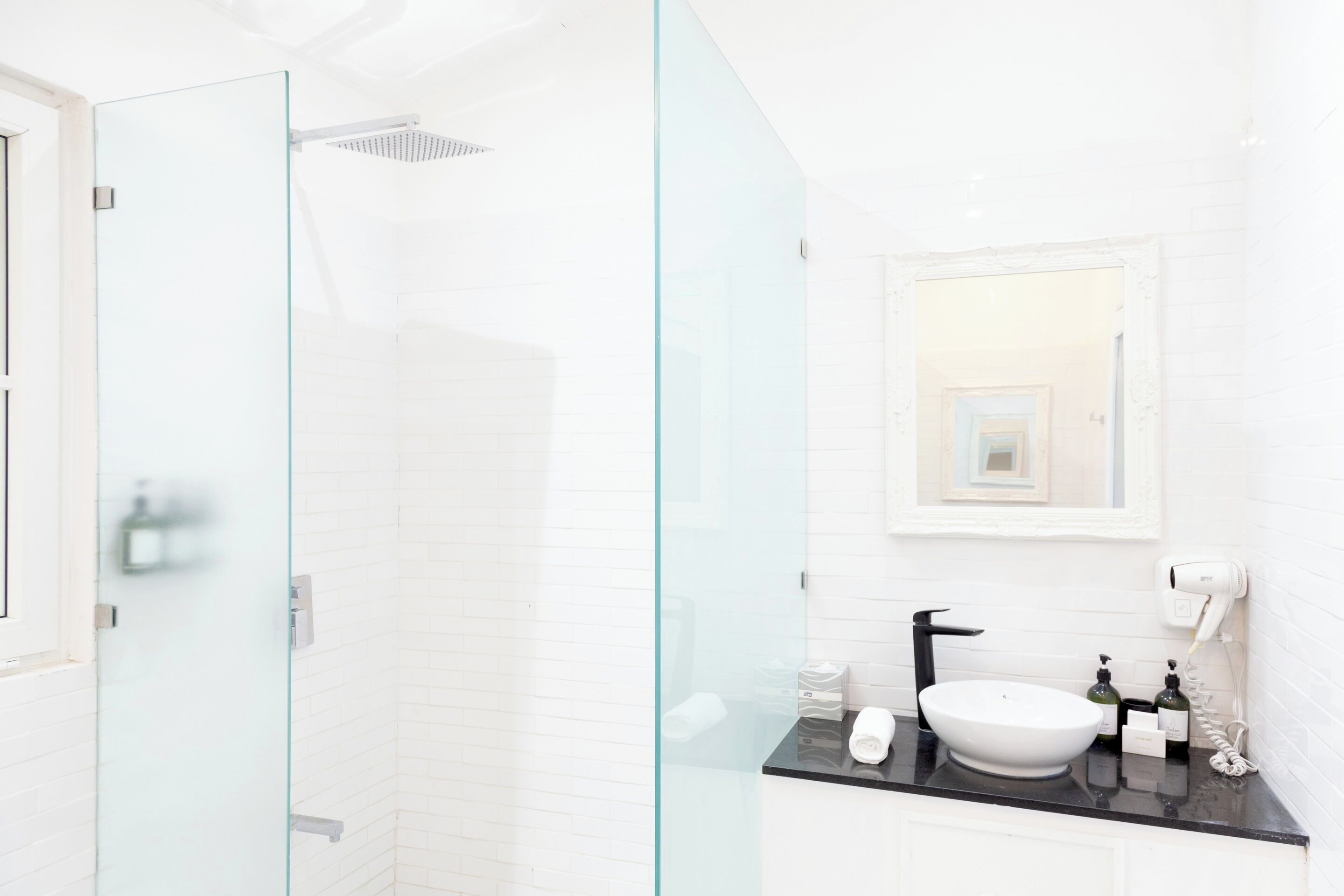 Un baño moderno con ducha envuelta en vidrio, un lavamanos blanco con grifo negro y un espejo sobre el lavamanos.