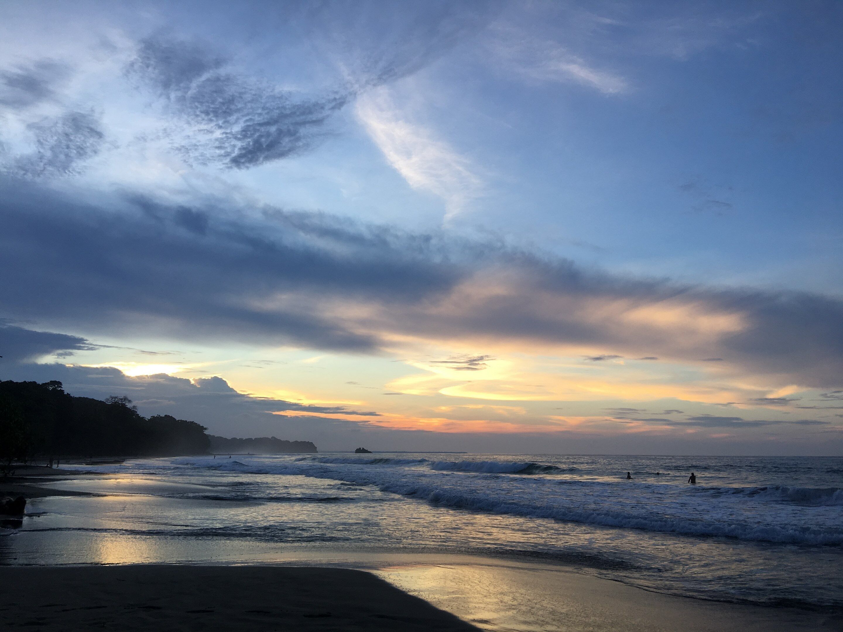 A beach with waves, a sunset, and a distant mountain.