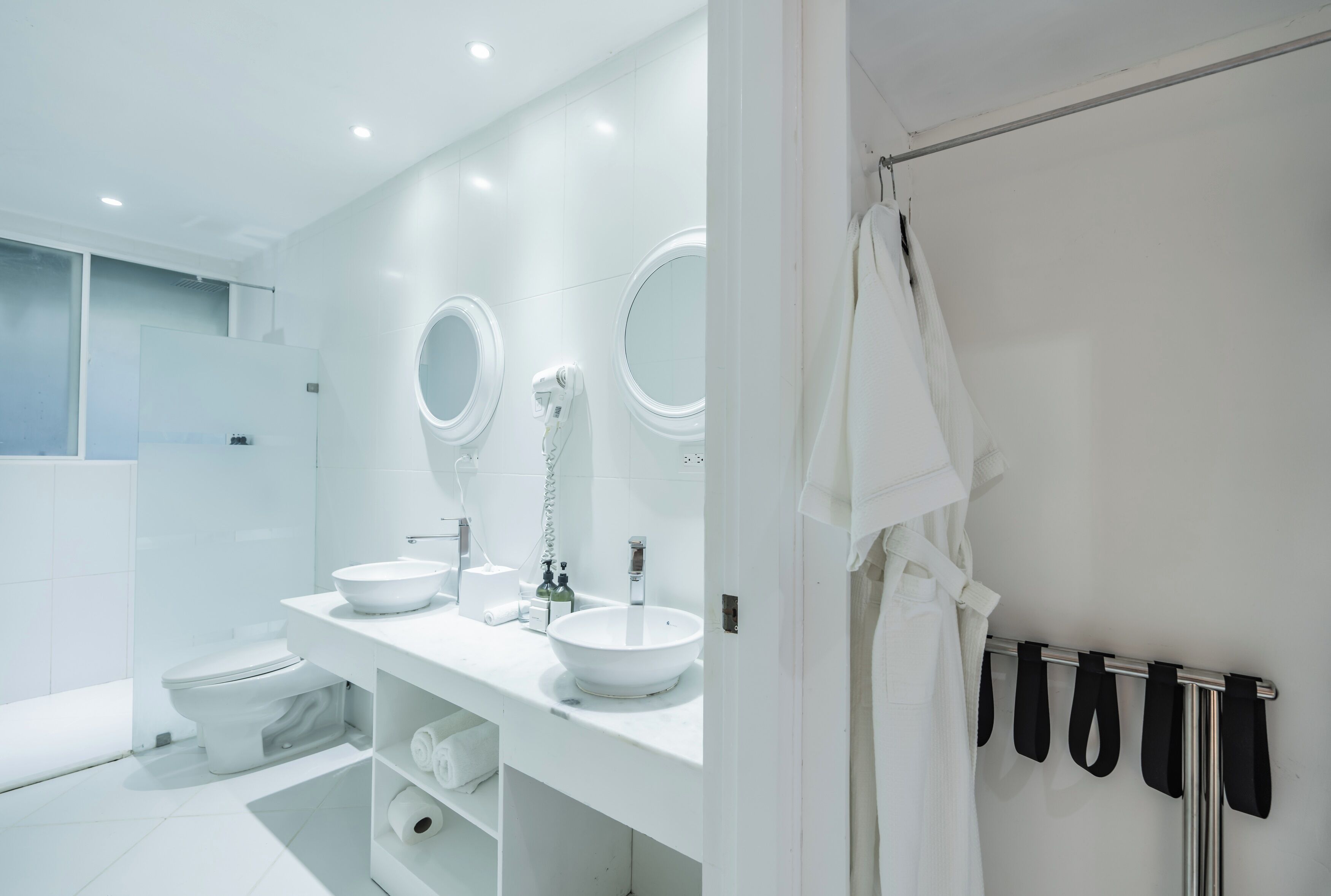 A modern bathroom with a white sink, two round mirrors, a toilet, and a towel rack.