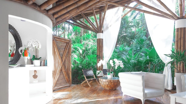 A room with a wooden floor, white furniture, a bamboo ceiling, and lush green plants. - Le Cameleon Puerto Viejo (Cahuita)