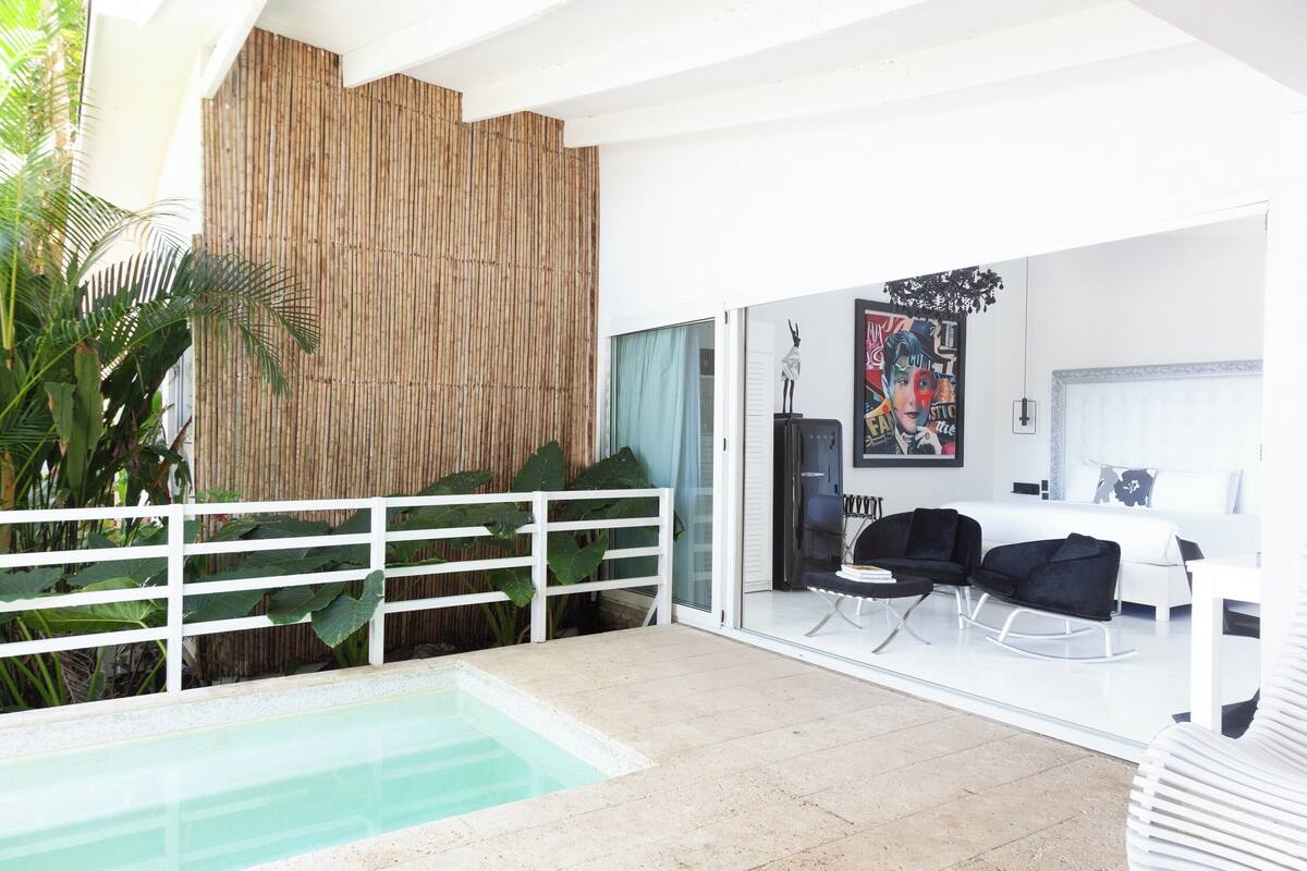 A modern living room with a pool, white furniture, and a bamboo wall.