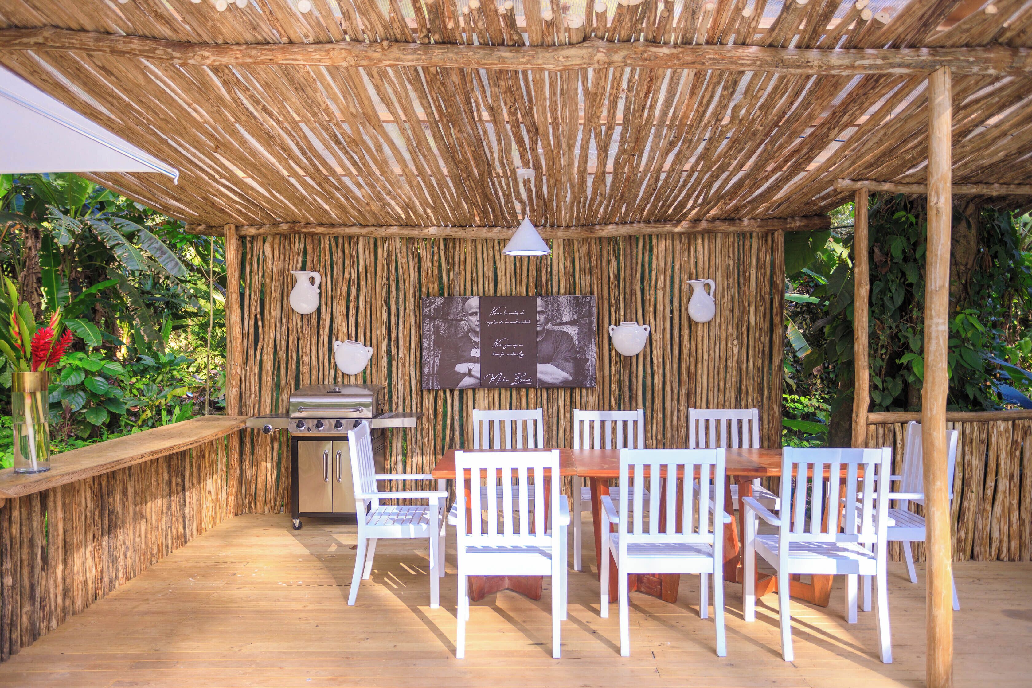 An outdoor patio with a wooden table and white chairs, a grill, and a wall-mounted sign.