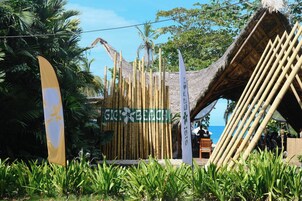 A beachside resort with a bamboo structure, a beach sign, and lush greenery.