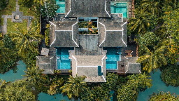 Ein Luftbild eines Resorts mit mehreren Schwimmbecken, umgeben von üppiger Vegetation und Palmen.