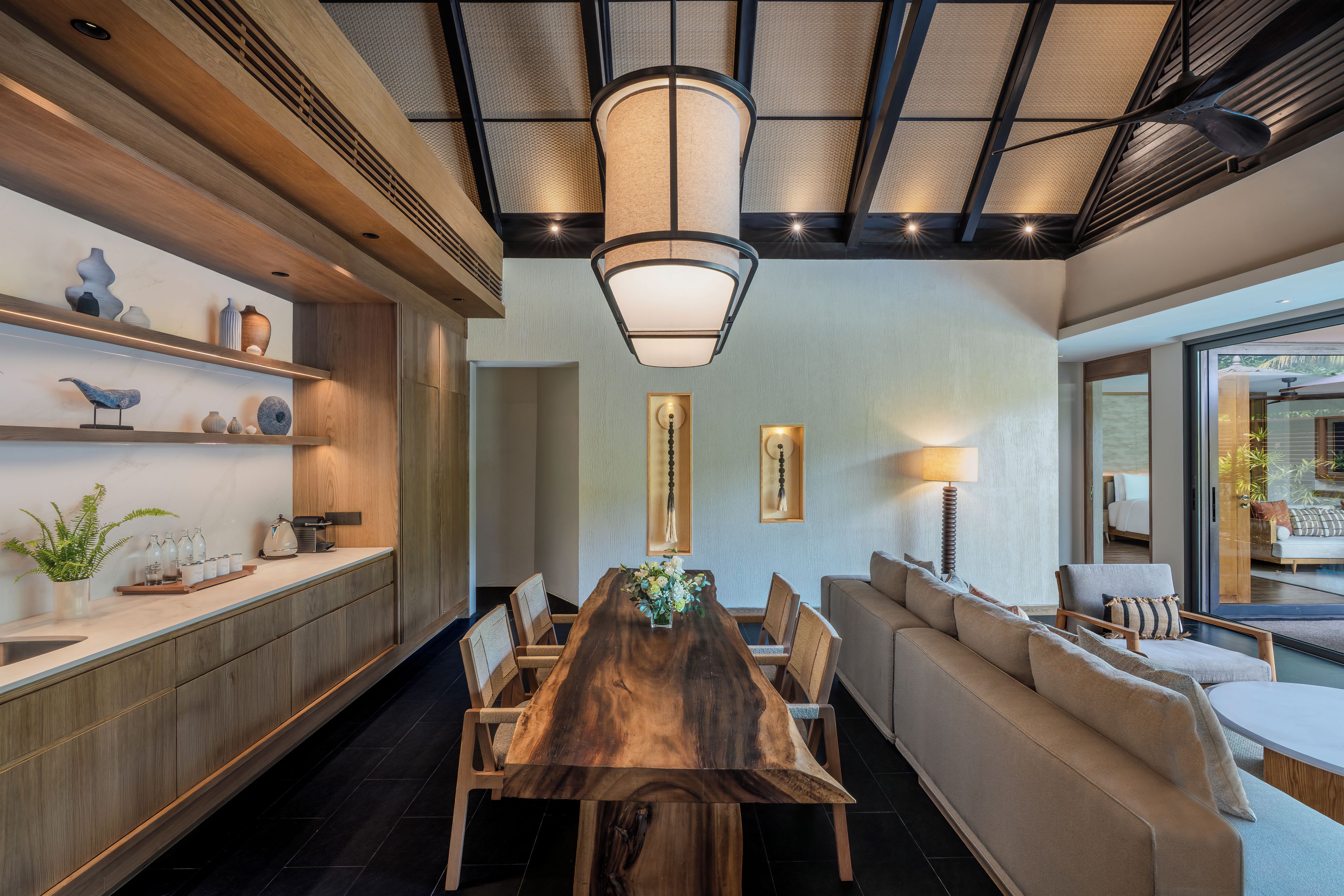 A modern dining area with a wooden table and chairs, a sofa, and a large window.