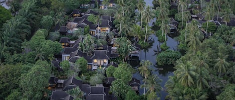 An aerial view of a resort with multiple bungalow-style buildings surrounded by dense tropical vegetation and a waterway.