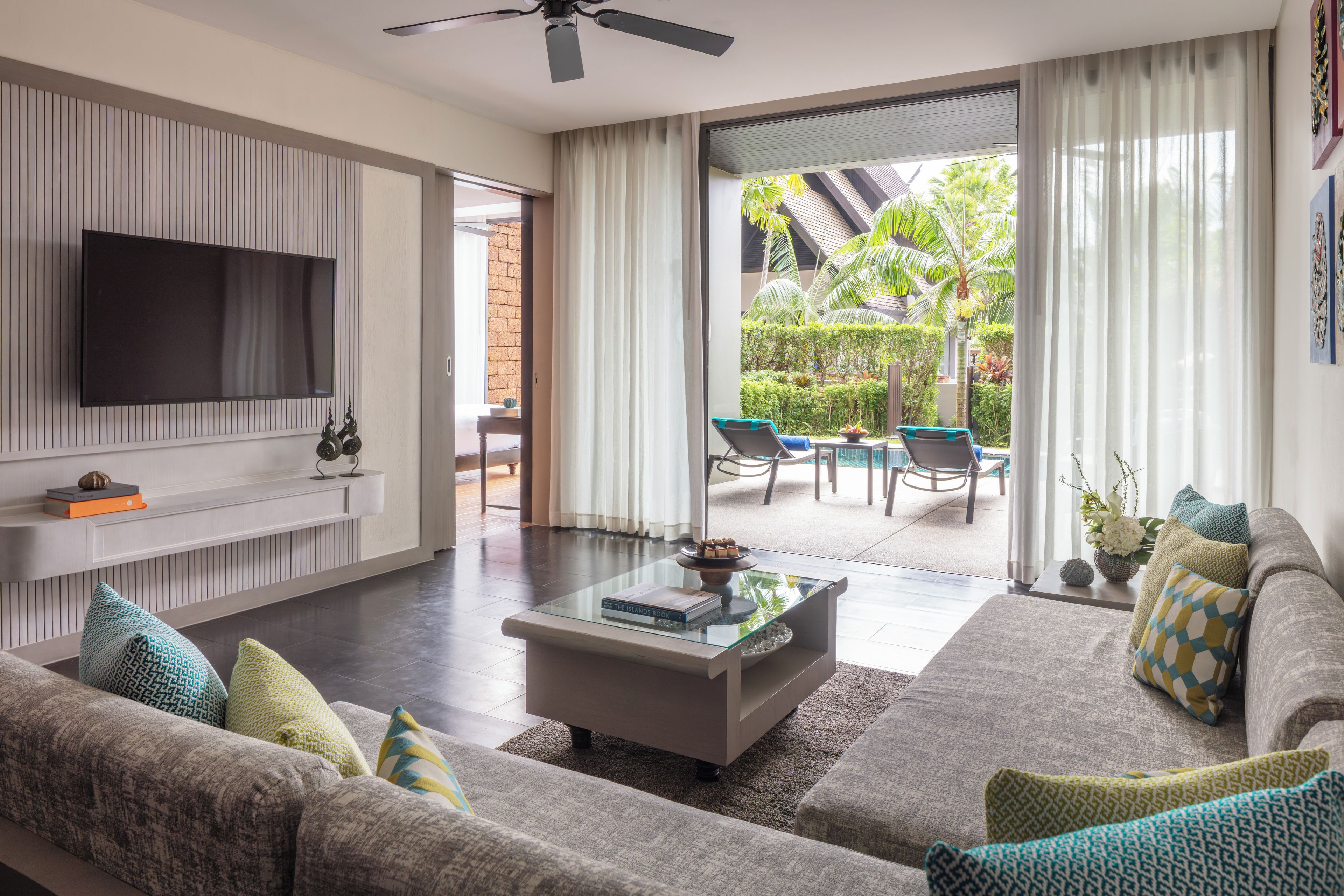 A modern living room with a flat-screen TV, a glass coffee table, and a sofa with patterned cushions.