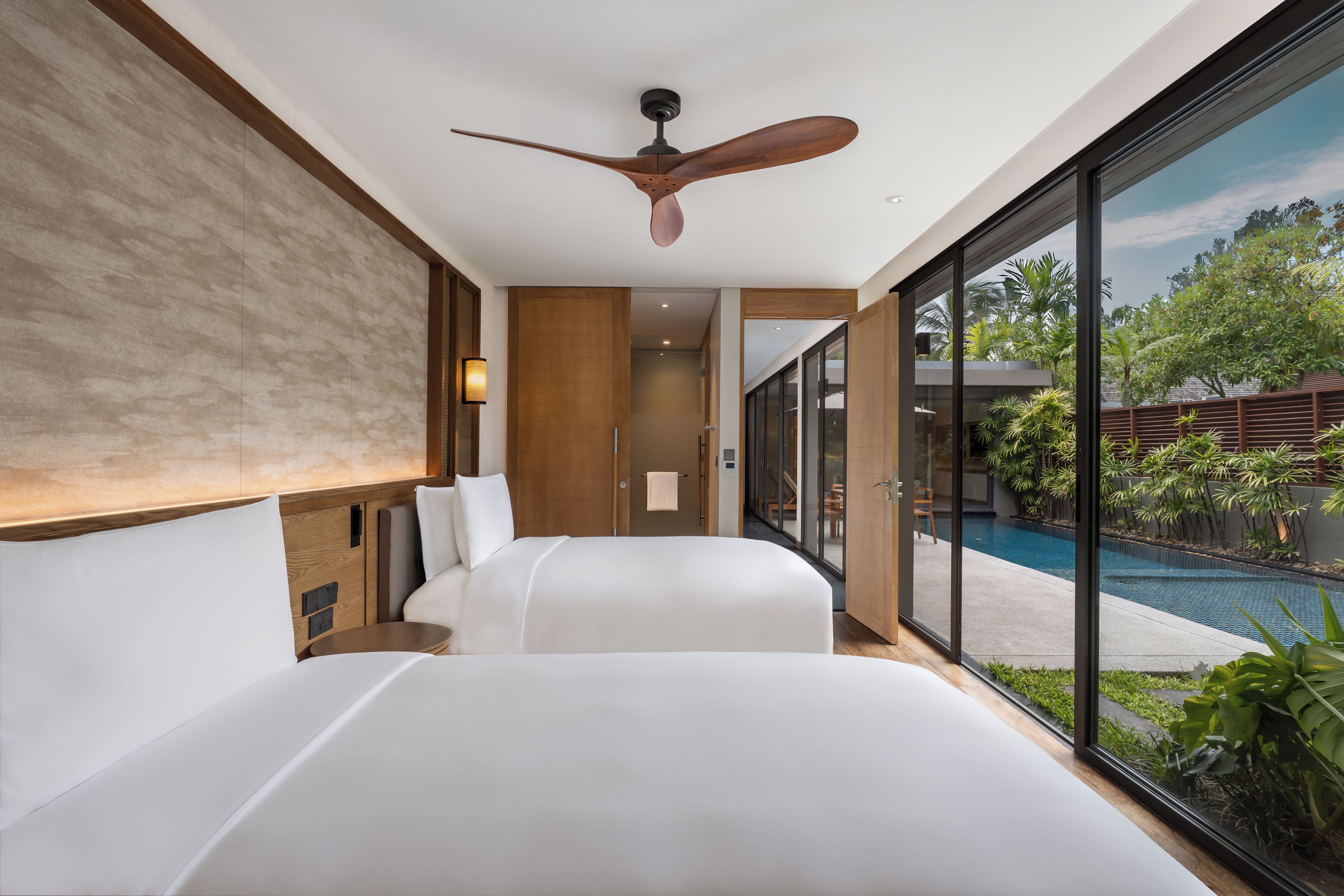 Une chambre d’hôtel moderne avec un grand lit, un ventilateur de plafond et une vue sur une piscine.